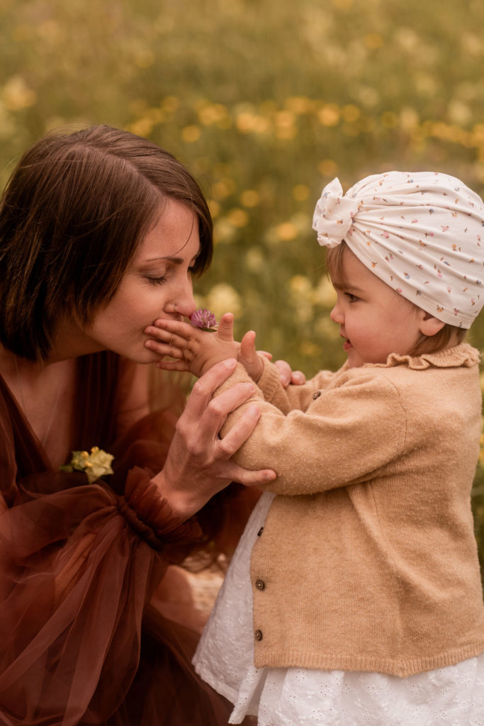 Kleines Mädchen auf einer Wiese mit ihrer Mummy hält Blume an die Nase von Ihrer Mama