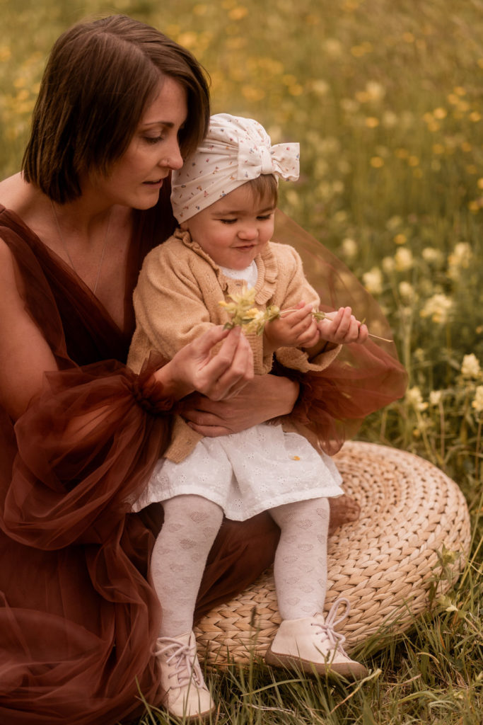Kleines Mädchen sitzt auf dem Schoß ihr Mutter, beide sitzen in einer Wiese bei einem Mummy-and-me-Shooting von PIC@MO mit Mona von Malm